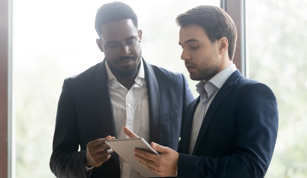 two men in blue jackets viewing computer tablet