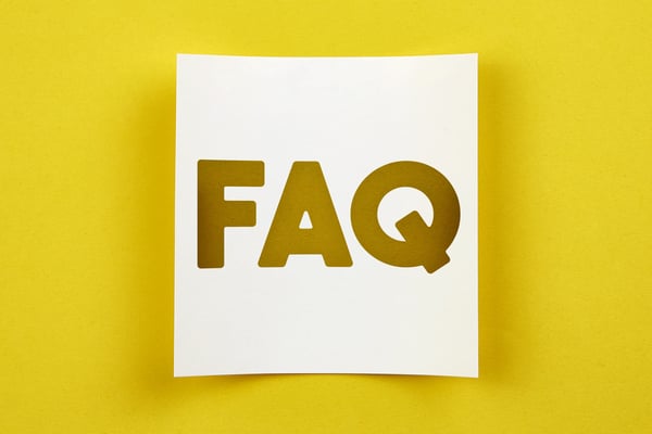 The letters FAQ cut out of a white background that is resting on a bright yellow background.