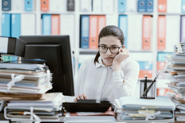 Female office worker at her desk overwhelmed by paper files