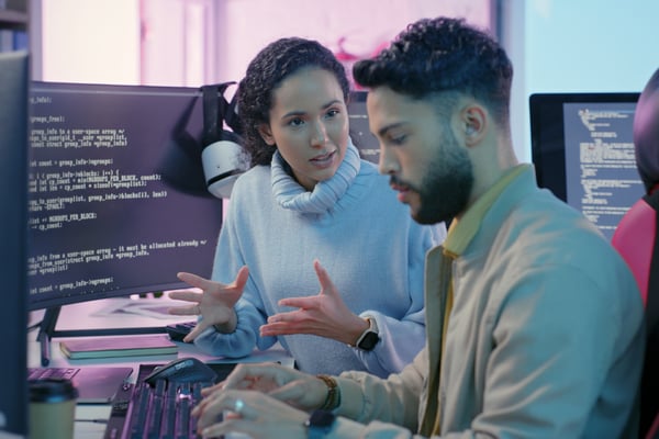 Hombre y mujer sentados delante de ordenadores discutiendo sobre estrategia de datos