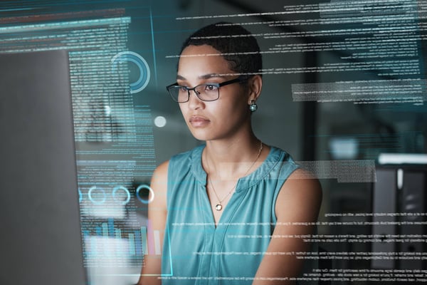 Businesswoman at a computer reviewing data shown on a futuristic overlay