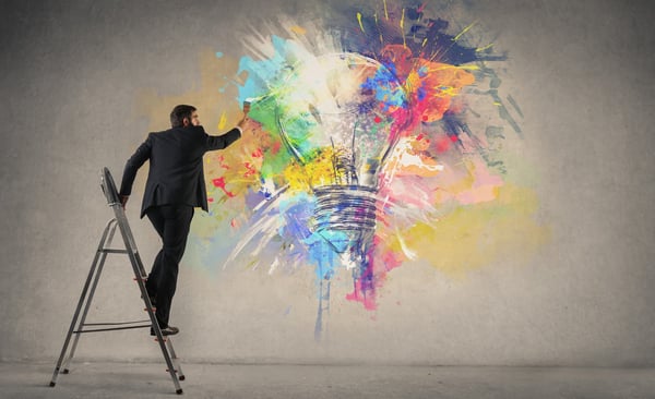 Man on ladder drawing a colorful lightbulb to represent innovative employees
