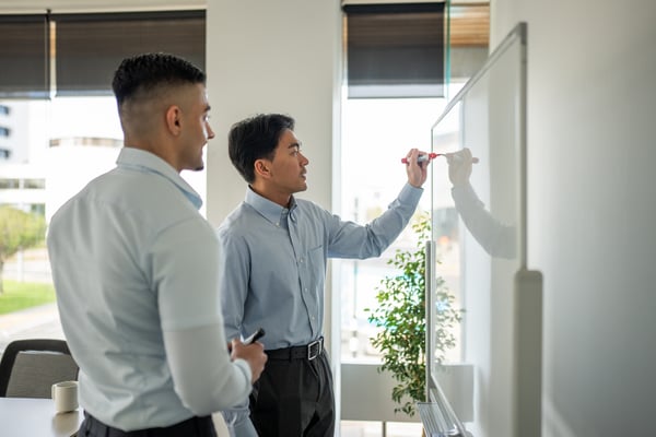 A young businessman drawing on a white board as a colleague watches