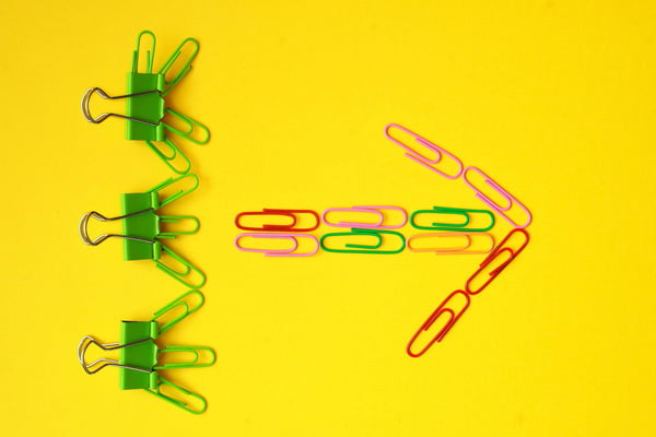 Clamped green paper clips with multi-colored paper clips forming an arrow