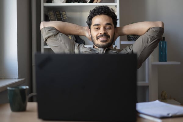 Young business man sitting at a computer looks pleased to have completed a job successfully