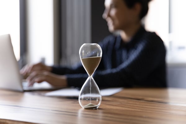 Close up hourglass measuring time, standing on wooden office table, businesswoman working on background 
