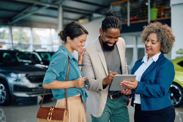 Couple with car saleswoman in a showroom sign a contract on a tablet