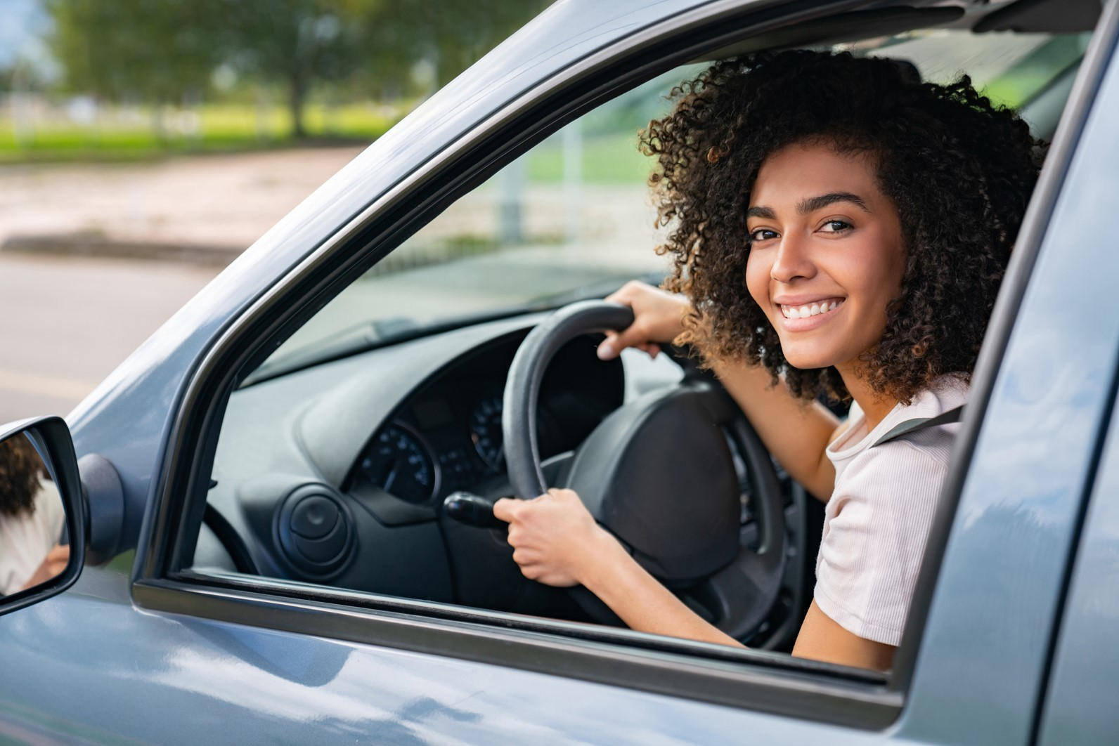 A happy young woman driving her car and smiling at the camera through the window