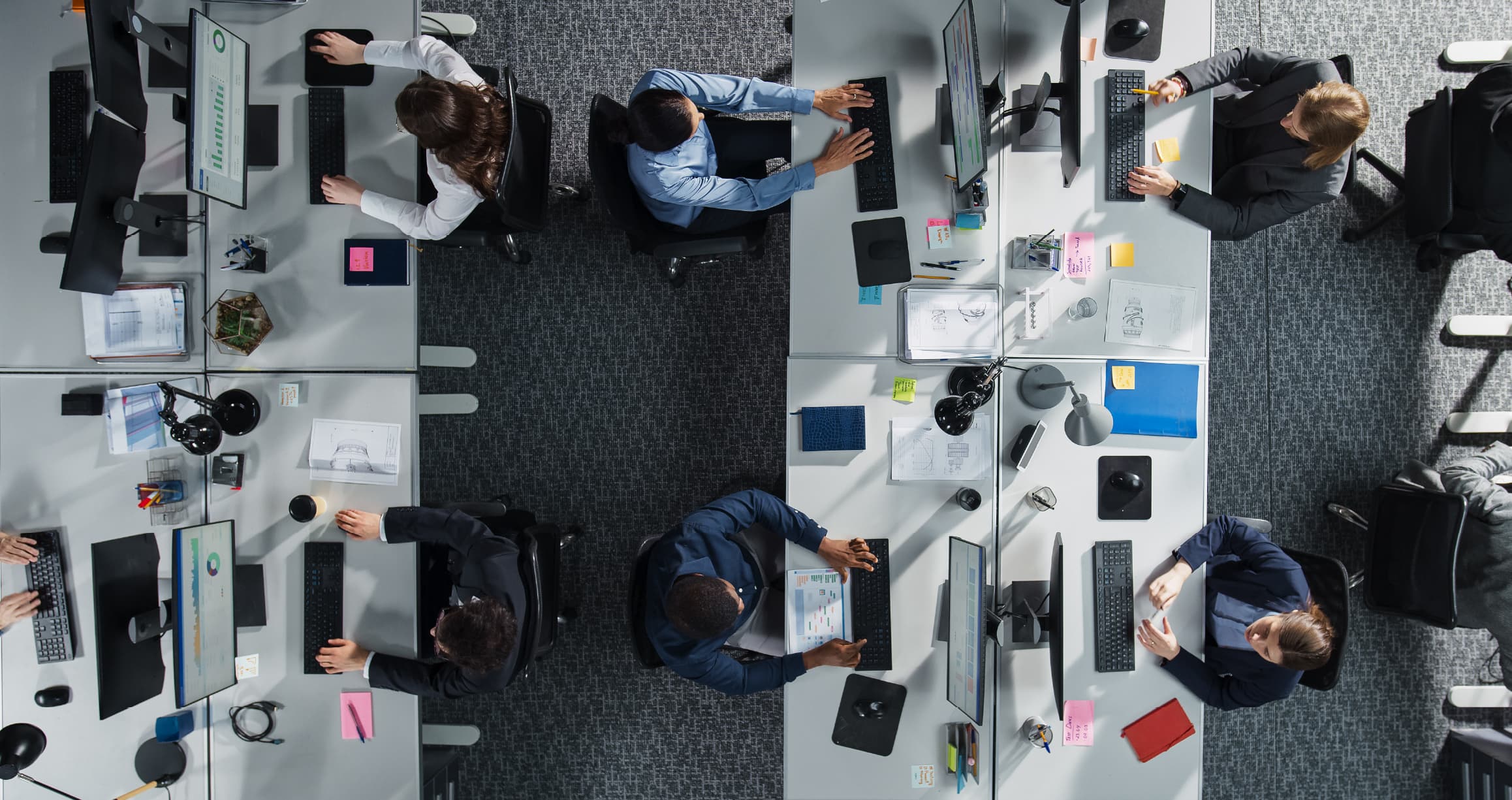 Overhead view of IT team members working at individual workstations in a modern office, illustrating the complexity of managing user access across multiple systems