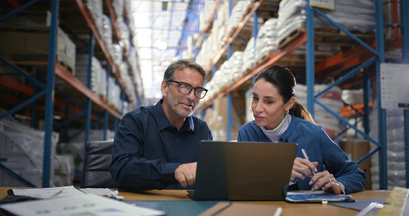 2 employees at desk looking at laptop while sitting in manufacturing factory